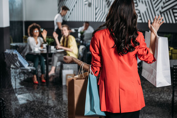 woman with shopping bags going to her friends in cafe