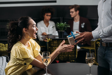 happy emotional woman taking gift from boyfriend at restaurant
