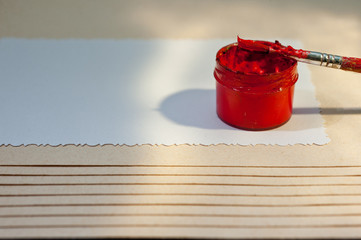 A jar with red paint and a brush on a sheet of white paper