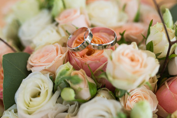 Two wedding golden rings lying on a wedding bouquets with orange and beige roses. Wedding details