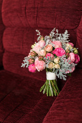 Wedding bouquet with purple and pink roses lying on a red armchair