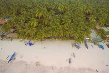 Aerial view of beautiful coastline of Indian ocean with tropical forest, sandy beach, calm blue water and fishing boats in Goa, Palolem beach