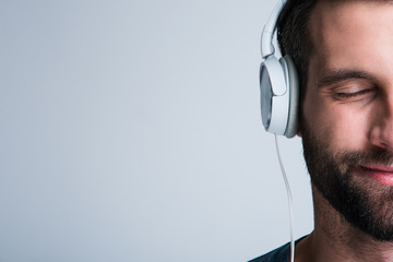 Perfect song. Part of portrait of handsome young man listening to music in headphones with smile...