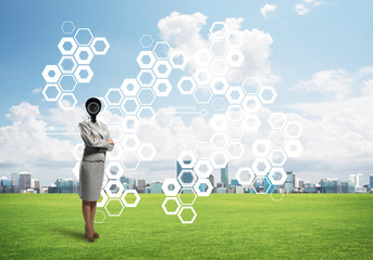 Camera headed woman standing on green grass against modern cityscape