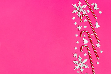 Christmas candy cane lied evenly in row on pink background with decorative snowflake and star. Flat lay and top view