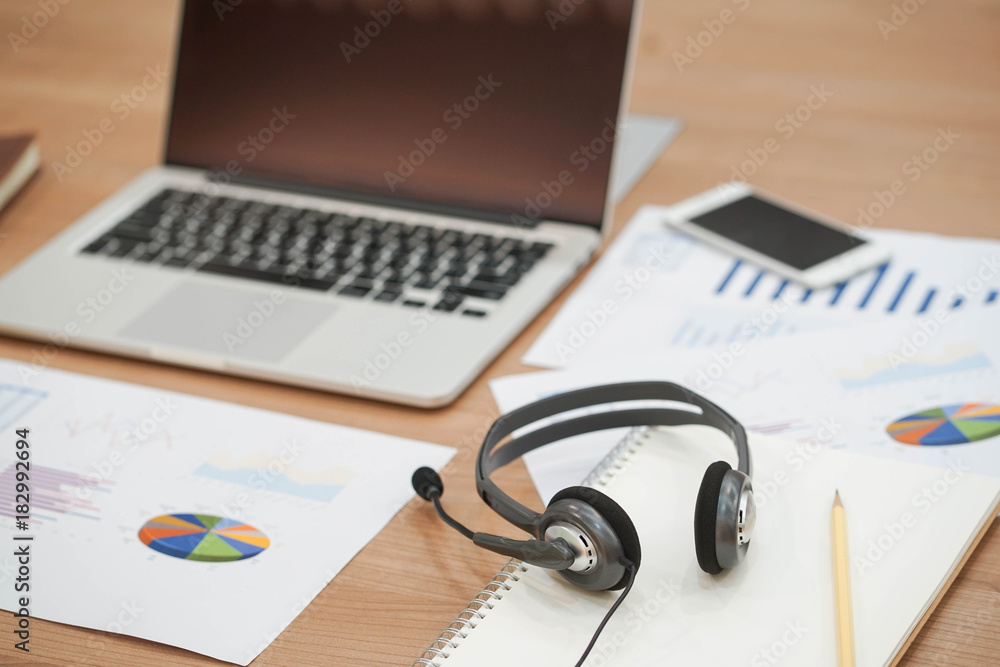 Wall mural close up of headset of call centre hotline at office desk with laptop and document paper,multitasking concept