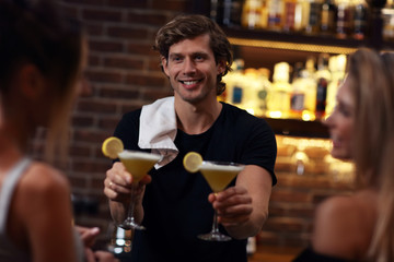 Handsome bartender serving cocktails in a pub