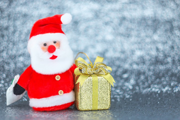 Santa claus doll and golden gift box with bokeh background.