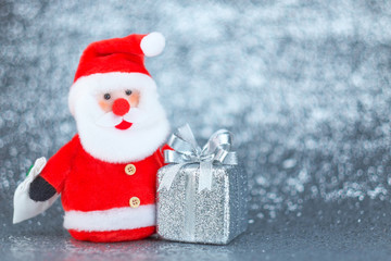 Santa claus doll and silver gift box with bokeh background.