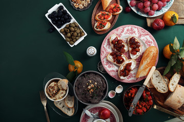 Set of various unusual appetizers: pate, olives, hummus, marinated plums with soft cheese on baguette and chiabatta slices. Old painters lighting style. Copy space