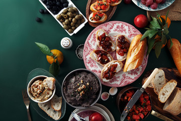 Set of various unusual appetizers: pate, olives, hummus, marinated plums with soft cheese on baguette and chiabatta slices. Old painters lighting style. Copy space