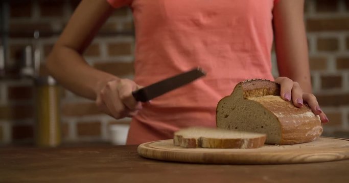 Woman hands cutting bread with knife on home kitchen 4k close-up video. Female slicing brown loaf to pieces. 