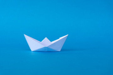 Business concept - paper ship origami on blue background.