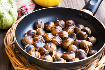 Roasted chestnuts in a pan top view with autumn dried leaves , cones and pumpkins, fall food , edible chestnuts