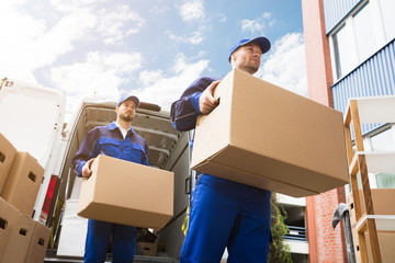 Close-up Of Two Delivery Men Carrying Cardboard Box - obrazy, fototapety, plakaty