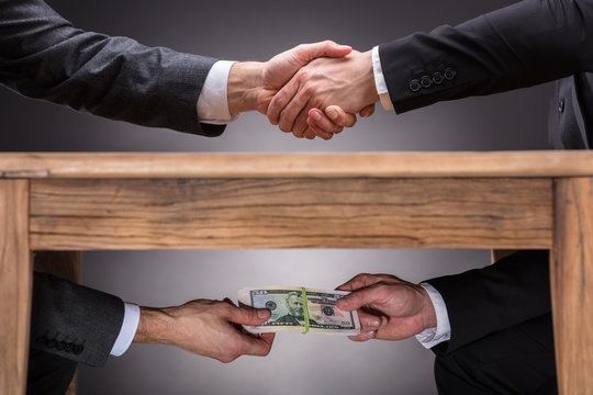 Businesspeople Shaking Hands And Taking Bribe Under Table