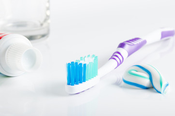 Toothbrush, tube of toothpaste and a glass in the background
