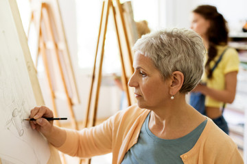 senior woman drawing on easel at art school studio
