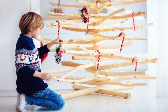 cute boy, kid decorate handcrafted christmas tree made of driftwood at home