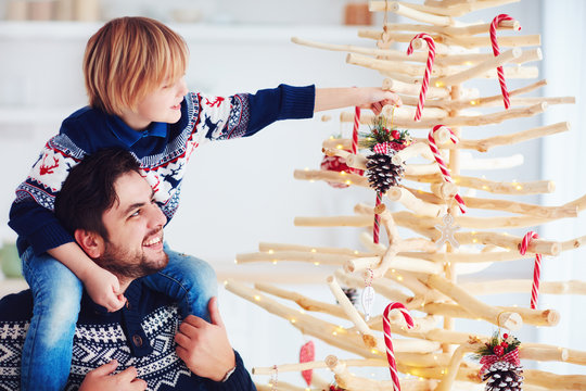 happy family, father and son decorate handcrafted christmas tree made of driftwood at home