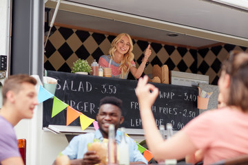 happy saleswoman showing thumbs up at food truck