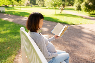 happy pregnant asian woman reading book at park