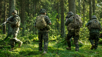 Squad of Five Fully Equipped Soldiers in Camouflage on a Reconnaissance Military Mission, Rifles in Firing Position. They're Moving in Formation Through Dense Forest. Back View Shot.
