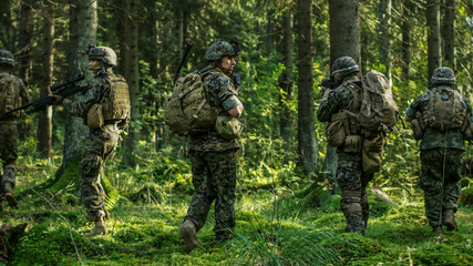Squad of Five Fully Equipped Soldiers in Camouflage on a Reconnaissance Military Mission, Rifles in Firing Position. They're Moving in Formation Through Dense Forest. Back View Shot.