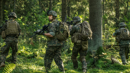 Fototapeta premium Squad of Fully Equipped Soldiers in Camouflage on a Reconnaissance Military Mission, Rifles in Firing Position. They're Moving in Formation Through Dense Forest. Back View Shot.