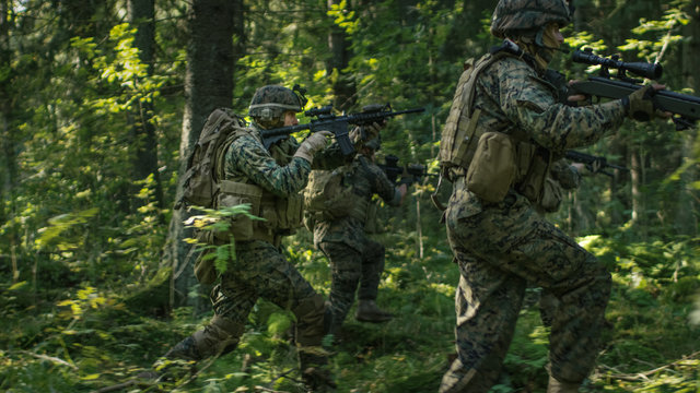 Squad of Fully Equipped Soldiers in Camouflage on a Reconnaissance Military Mission, Rifles in Firing Position. They're Running in Formation Through Dense Forest.