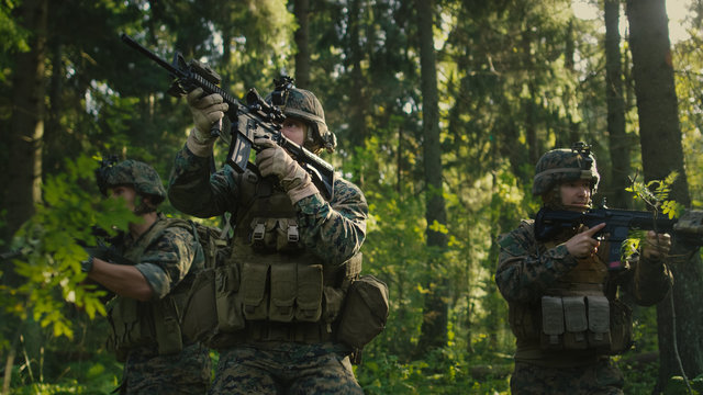Three Fully Equipped Soldiers Wearing Camouflage Uniform Attacking Enemy, They're in Shooting Ready Stance, Aiming Rifles. Military Operation in Action, Squad Standing in Dense Forest.
