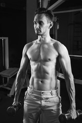 Handsome muscular man working out with dumbbells at gym. Bodybuilding, sport and fitness lifestyle. Black and white photo.