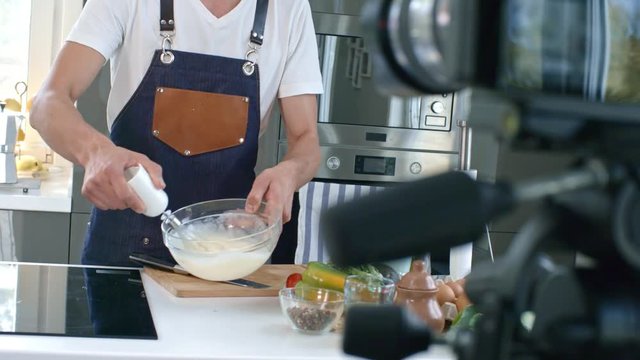 Handheld shot of laughing professional chef whisking mixture and talking during recording on cooking show