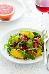 Fresh salad with arugula, orange, grapefruit, walnuts and pomegranate seeds on white table cloth. Healthy food.