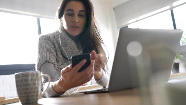Woman connected with laptop and smartphone, using earphones