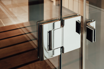 Close metal silver hinge is mounted on the glass construction of the door to the sauna, bathroom or...