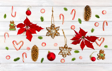 Christmas decoration. Flower of red poinsettia, branch christmas tree, christmas balls, gingerbread, candy canes and cones spruce on background of white painted wooden planks. Top view, flat lay.