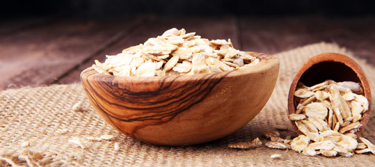 Oat flakes in bowl and wooden spoon on burlap.