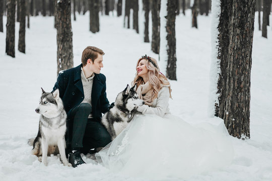 Groom is kissing his bride on the temple on the white snow background. Winter wedding. Artwork. Selective focus on the bouquet