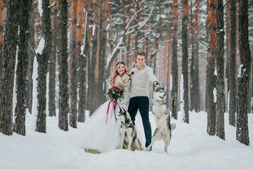 Fototapeta na wymiar Beautiful bride and groom with two siberian husky are posed on background of snowy forest. Artwork
