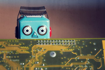 Vintage tin toy robot behind computer board, artificial intelligence concept