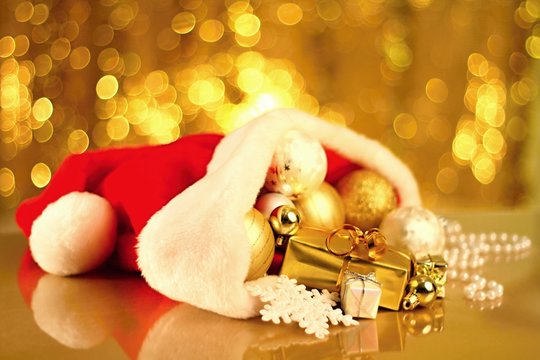 Christmas Image of presents taken on a shiny surface with a red hat and balls on gold background also it is sitting on a table top no people stock photo