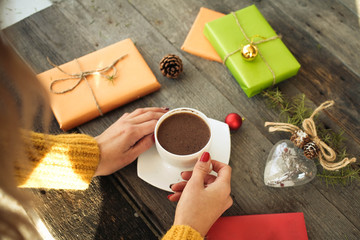 Opening Christmas present. Woman's hands holding a cup of hot coffee on rustic wooden table