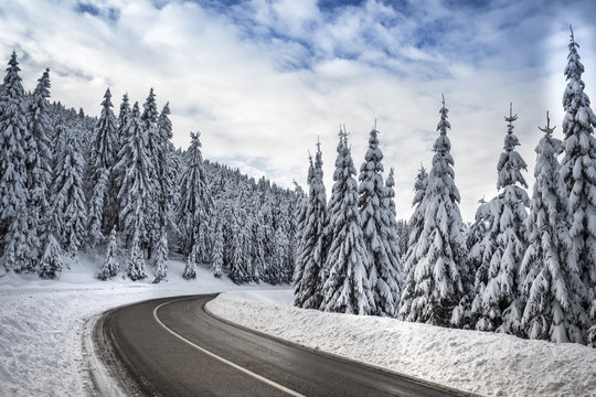 Curved snowy road in winter forest, blue sky, clouds