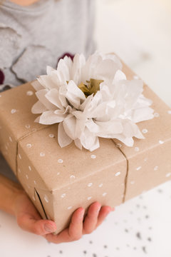 Closeup of Christmas, birthday or any other celebration gift wrapped in craft paper and decorated with ribbon and handmade paper flower in woman's hands