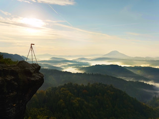 Tripod  with camera on view point ready for photography. Exposed rocky edge above landscape.