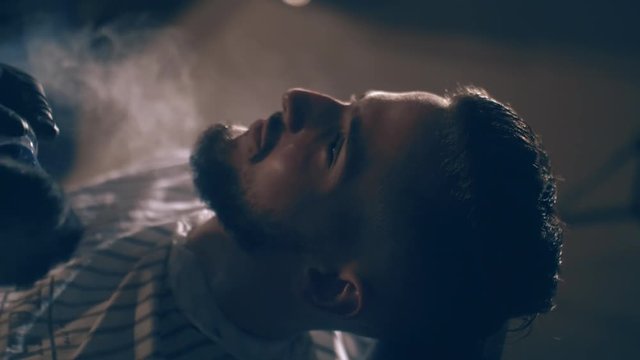 The barber shaves his head, mustache and beard to the man in the barbershop. The stylist uses a classic sharp razor, neatly shaving the client.