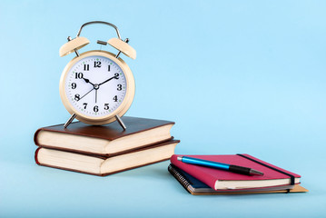 Old clock on books and notebook with pen isolated on a blue background, blog concept