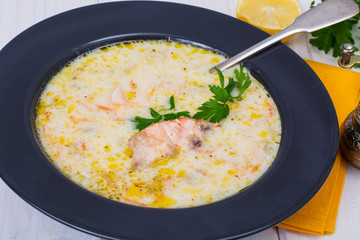 Creamy soup with salmon in black plate on white wooden table
