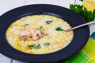 Creamy soup with salmon in black plate on white wooden table